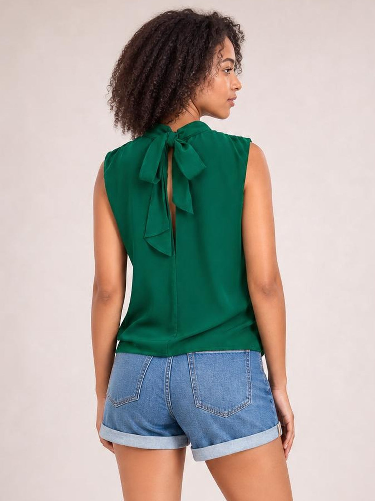 Model shown from the back wearing a solid green sleeveless mock neck blouse with a tied bow, regular straight silhouette, and smooth construction.