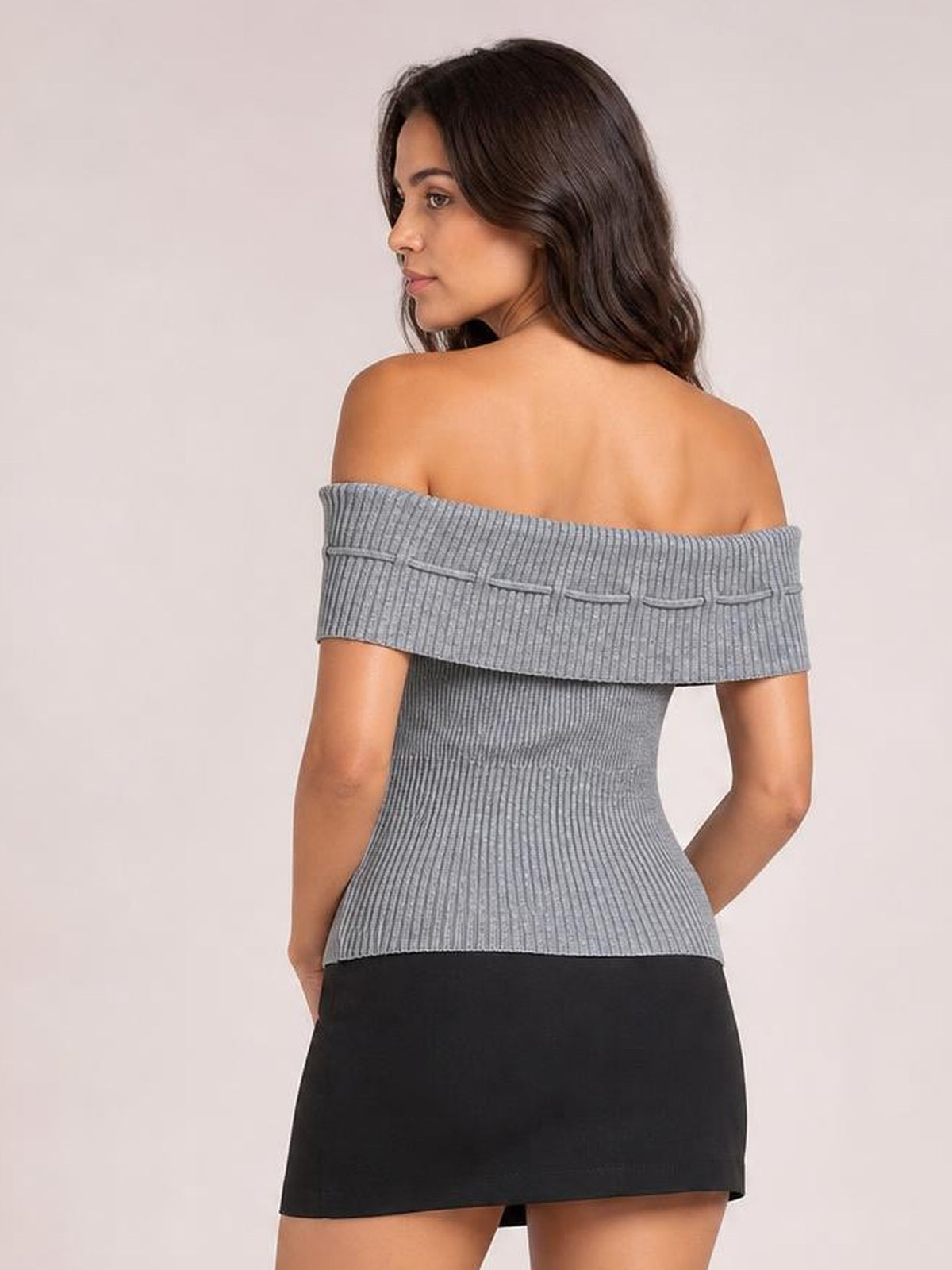 Model looks over her shoulder wearing a gray ribbed knit top with an off-shoulder neckline, short sleeves, tied back details, and a fitted silhouette.