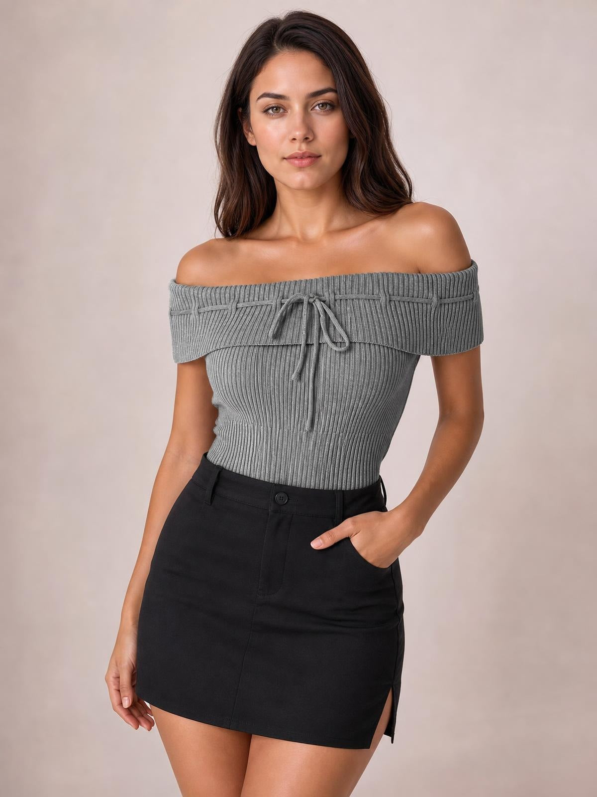 Model poses with one hand in her pocket wearing a gray ribbed tied off-shoulder short sleeve knit top with a fitted silhouette.