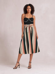 Model wears a tied striped spaghetti strap dress with a black fitted bodice, chain detail, multicolor vertical stripes, and a flared midi silhouette.