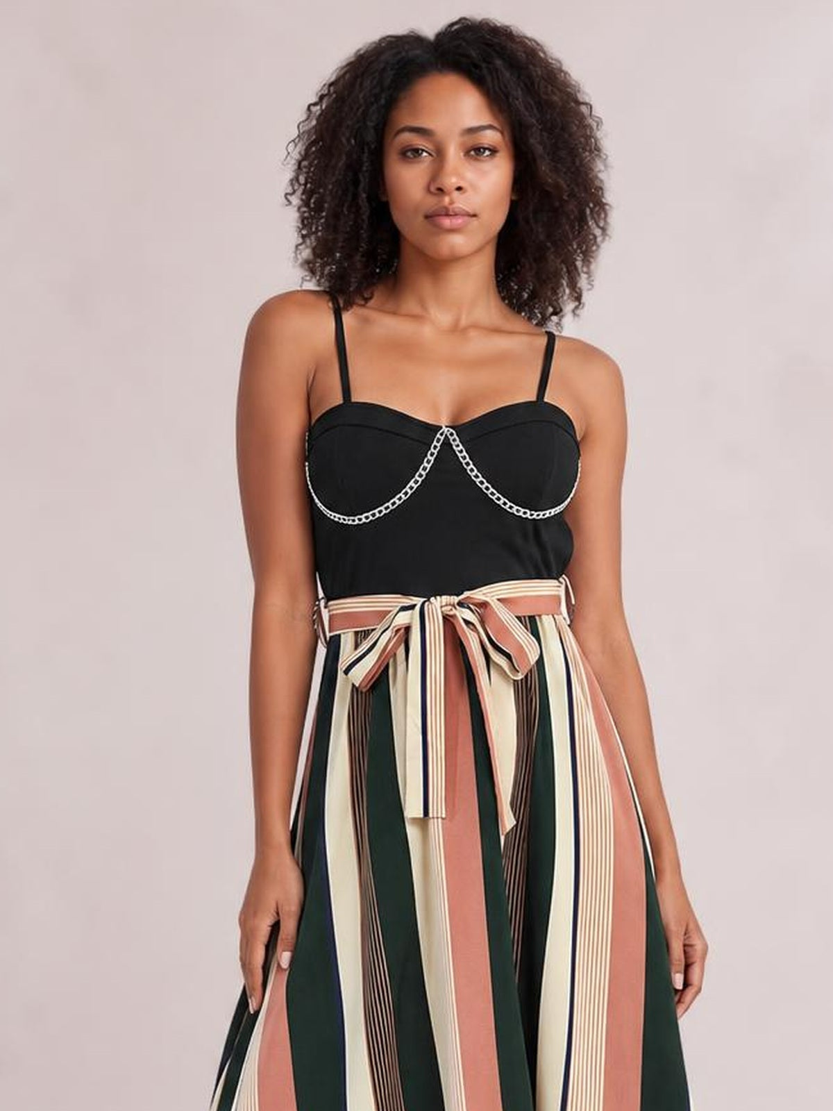 Front-facing model wears a black tied striped spaghetti strap dress with a fitted bodice, decorative trim, and a flowing multicolor vertically striped skirt.