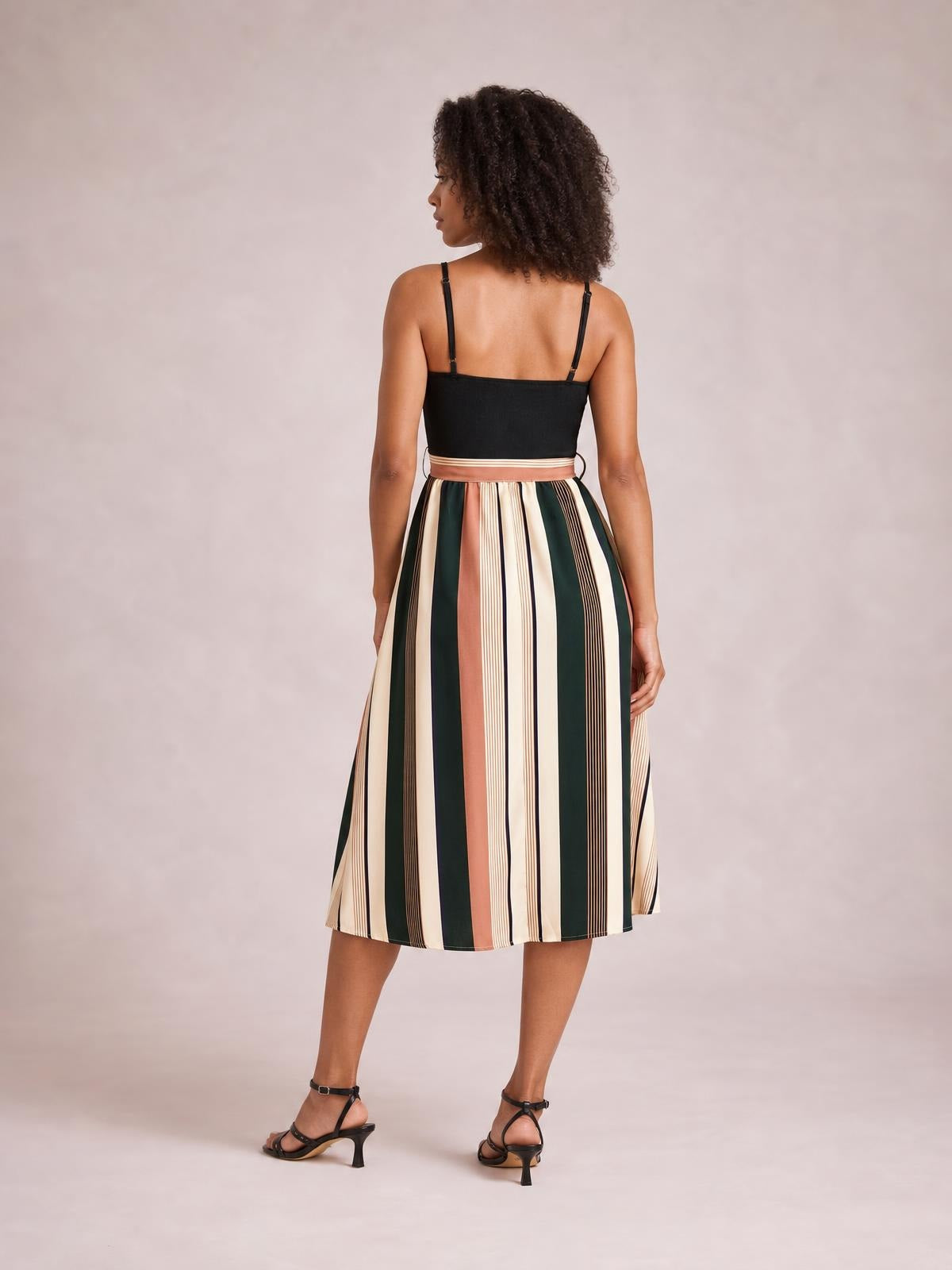 Model shown from behind wearing a tied striped spaghetti strap dress with a black bodice, defined waist, and multicolor vertical-striped midi skirt.