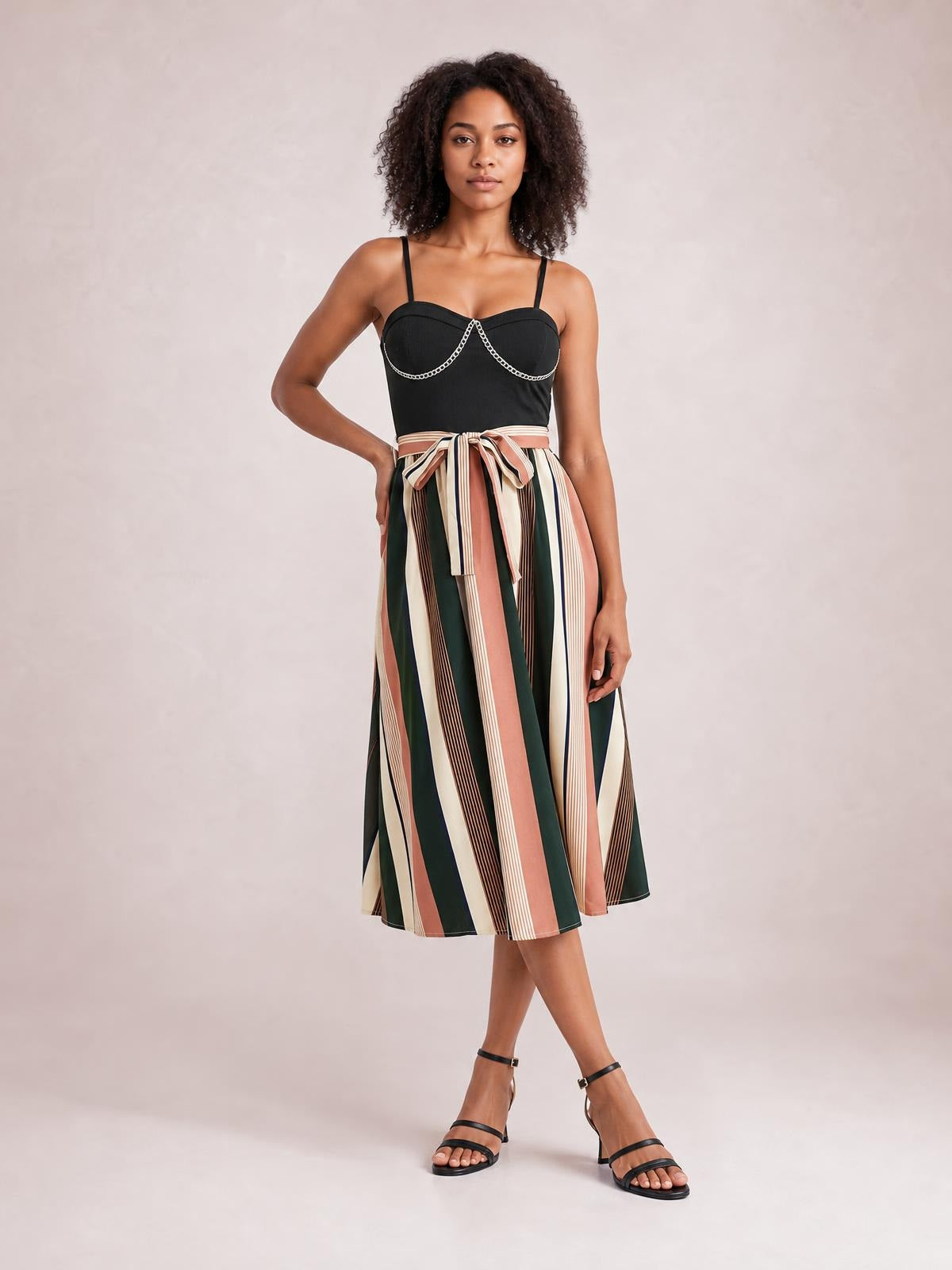 A model poses in a black spaghetti strap dress with a fitted bodice, tied waist, and flowing A-line midi skirt in multicolor vertical stripes.