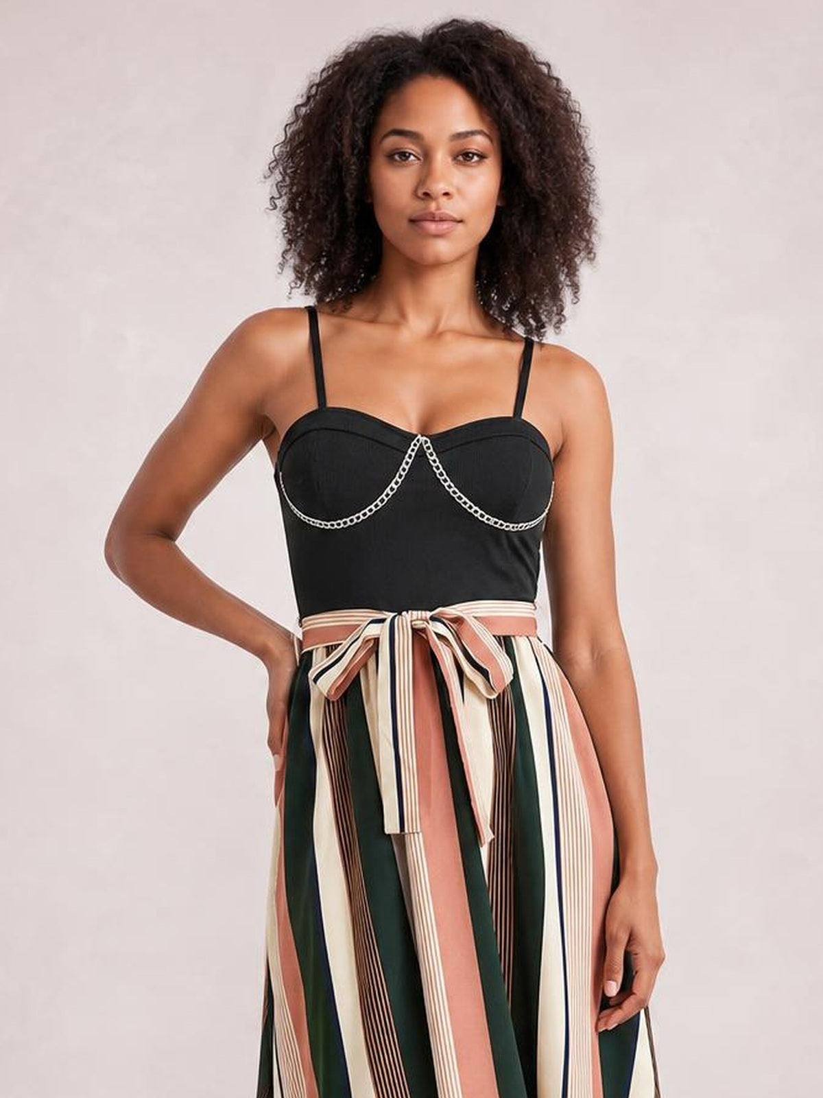 Model poses in a tied striped spaghetti strap dress with a black fitted bodice, decorative trim, and a flowing vertical-striped skirt.