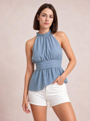 A model poses in a dusty blue Swiss dot tank with a ruffled mock neck, gathered bodice, wide tied waist, and softly flared peplum hem.