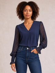 Model wears a navy V-neck top with a smooth opaque bodice and long sheer mesh sleeves featuring a chevron pattern, gathered cuffs, and a relaxed silhouette.