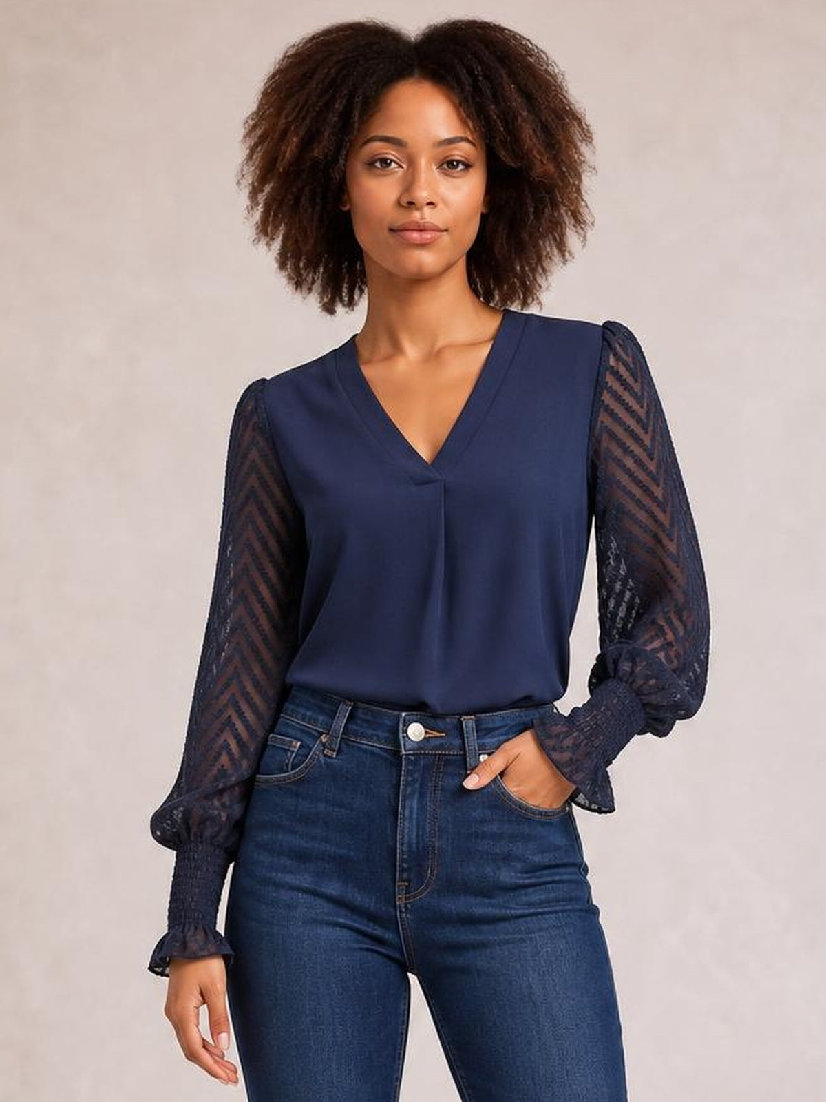 Model wears a navy V-neck top with a smooth opaque bodice and long sheer mesh sleeves featuring a chevron pattern, gathered cuffs, and a relaxed silhouette.