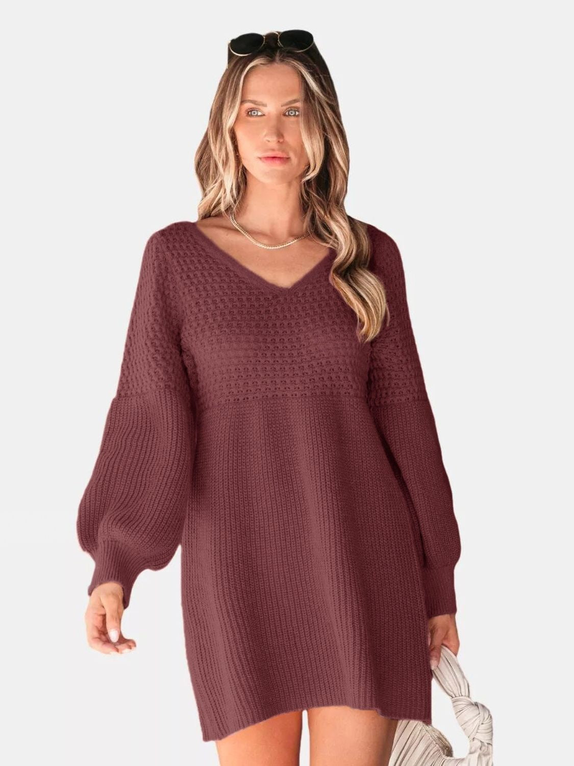 Model poses in a burgundy V-neck sweater dress with a relaxed above-knee silhouette, textured knit construction, and voluminous long sleeves with ribbed cuffs.