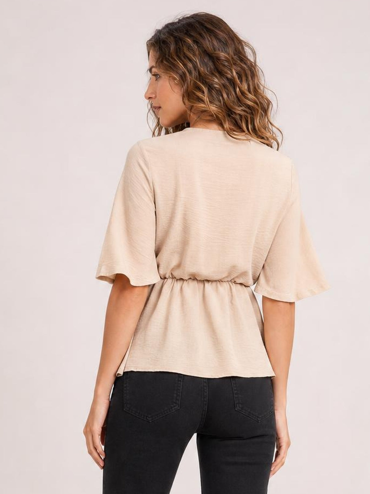 Model shown from behind wearing a solid cream blouse with half sleeves, a relaxed long silhouette, and a gathered waist detail above black jeans.