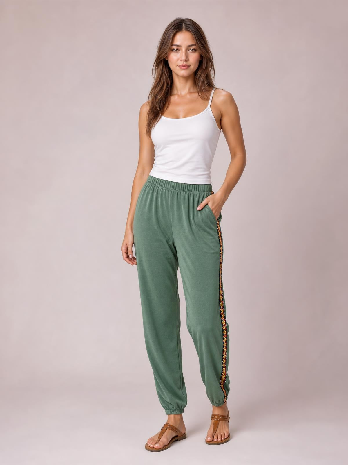 Model stands in sage green joggers with an elastic waist, relaxed tapered silhouette, ankle cuffs, and a multicolor weave band patchwork side stripe.