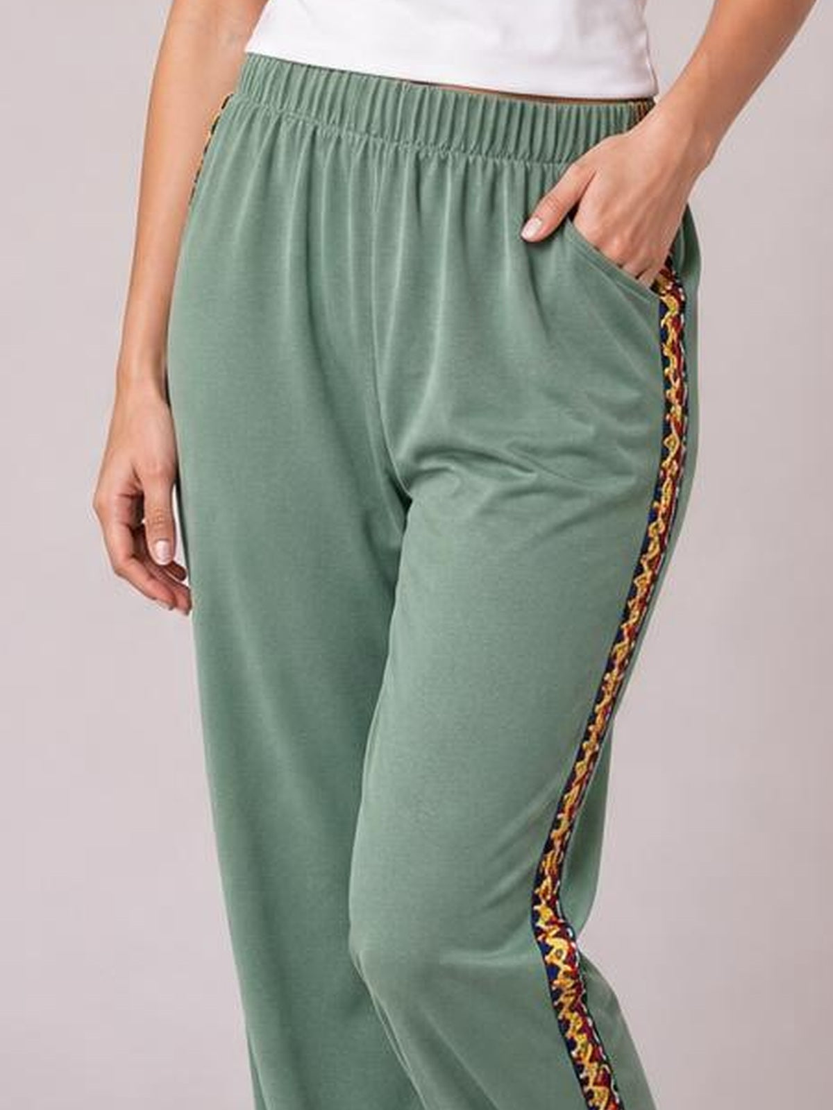 Model wearing sage green joggers with an elastic waist, relaxed silhouette, side pockets, and colorful woven band patchwork along the outer leg.