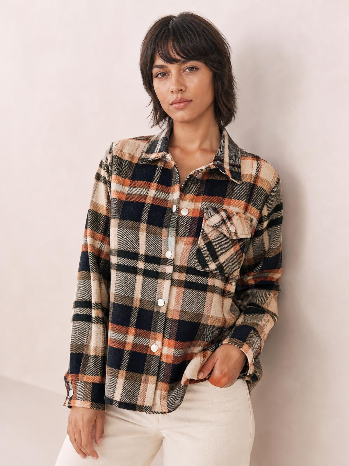 Model wearing a beige, black, and rust plaid button-front shirt jacket with a collared neckline, long dropped-shoulder sleeves, and flap breast pockets.