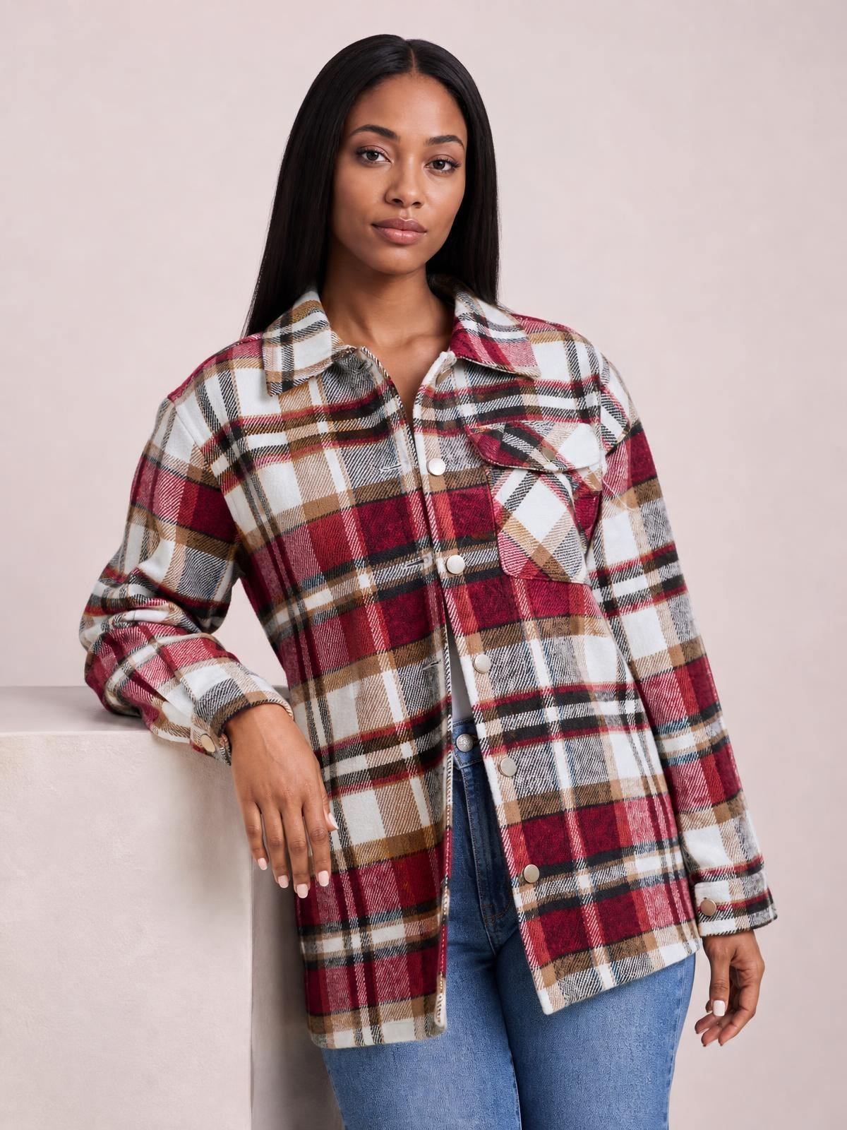 A model wears a relaxed red, white, tan, and black plaid button-front shirt jacket with a collared neck, dropped shoulders, long sleeves, and breast pockets.