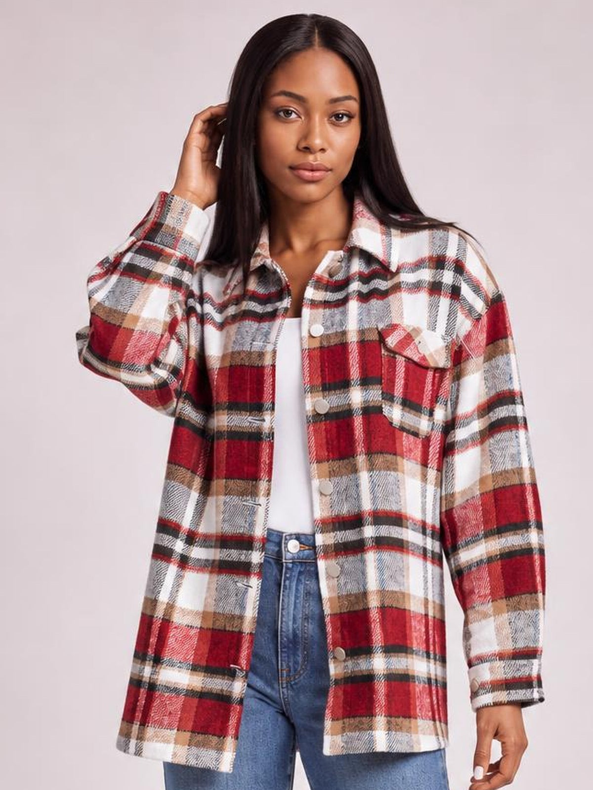 Model poses in a red, white, and black plaid button-front shirt jacket with a collared neckline, long dropped-shoulder sleeves, breast pockets, and an easy fit.