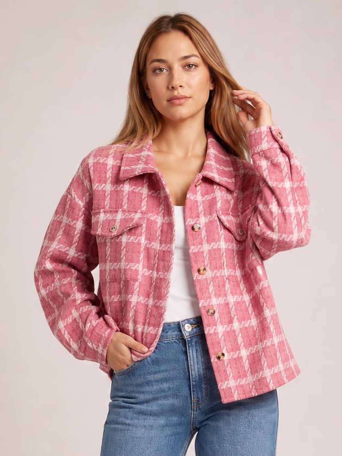 Model poses in a pink plaid button-up long sleeve jacket with a collared silhouette, front buttons, and flap pockets.