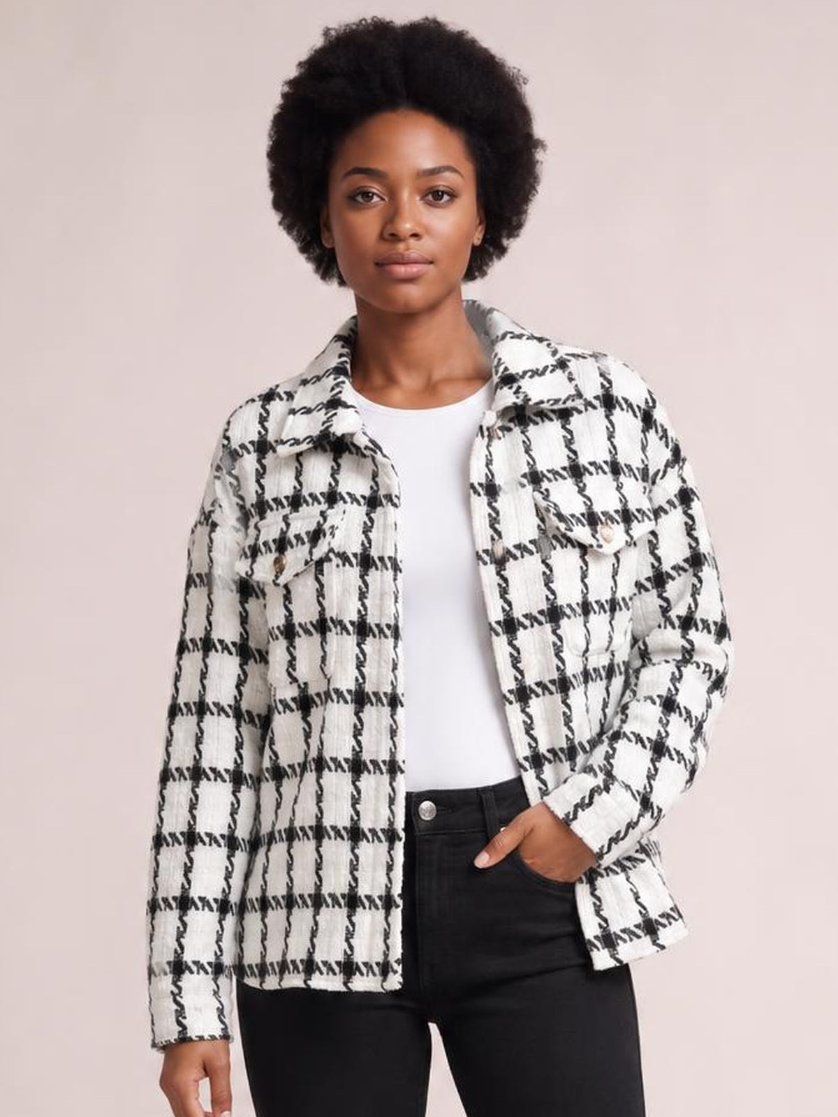 Model wearing a black-and-white plaid button-up long sleeve jacket with a collared silhouette, chest pockets, and one hand tucked into her jeans pocket.