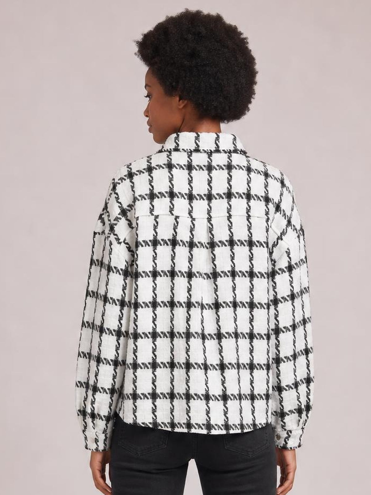 Model shown from the back in a white and black plaid button-up long sleeve jacket with a collared, straight silhouette and cuffed sleeves.