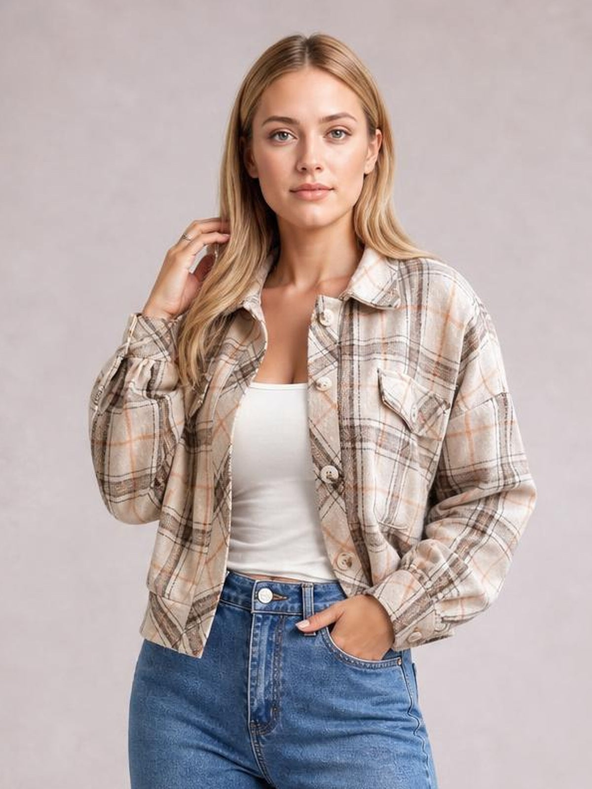 Model poses in a beige plaid button-up long sleeve jacket with a collared neckline, chest pockets, and relaxed cropped silhouette.