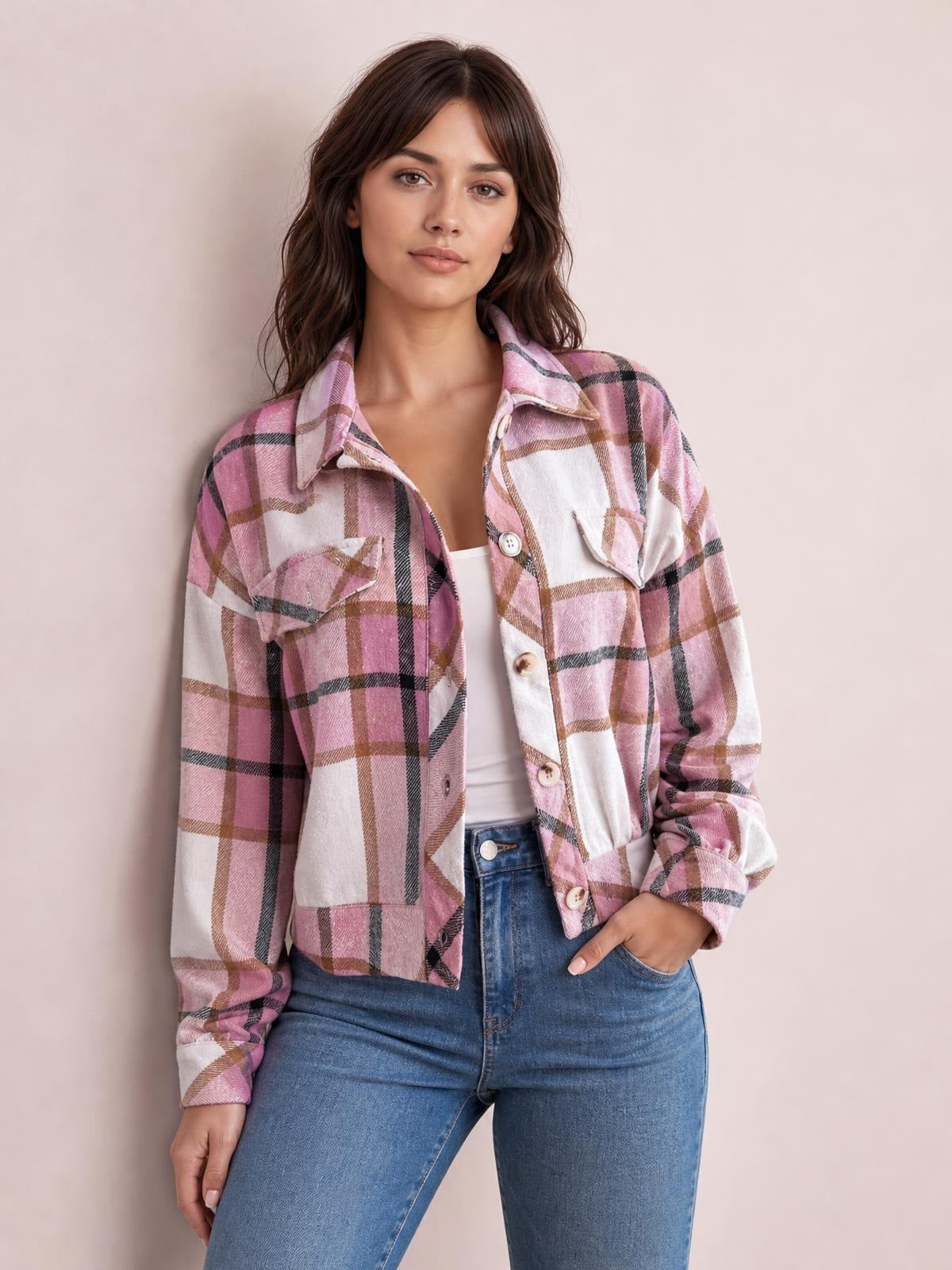 Model poses in a pink, white, and brown plaid button-up long sleeve jacket with a collared, cropped silhouette and chest flap pockets.