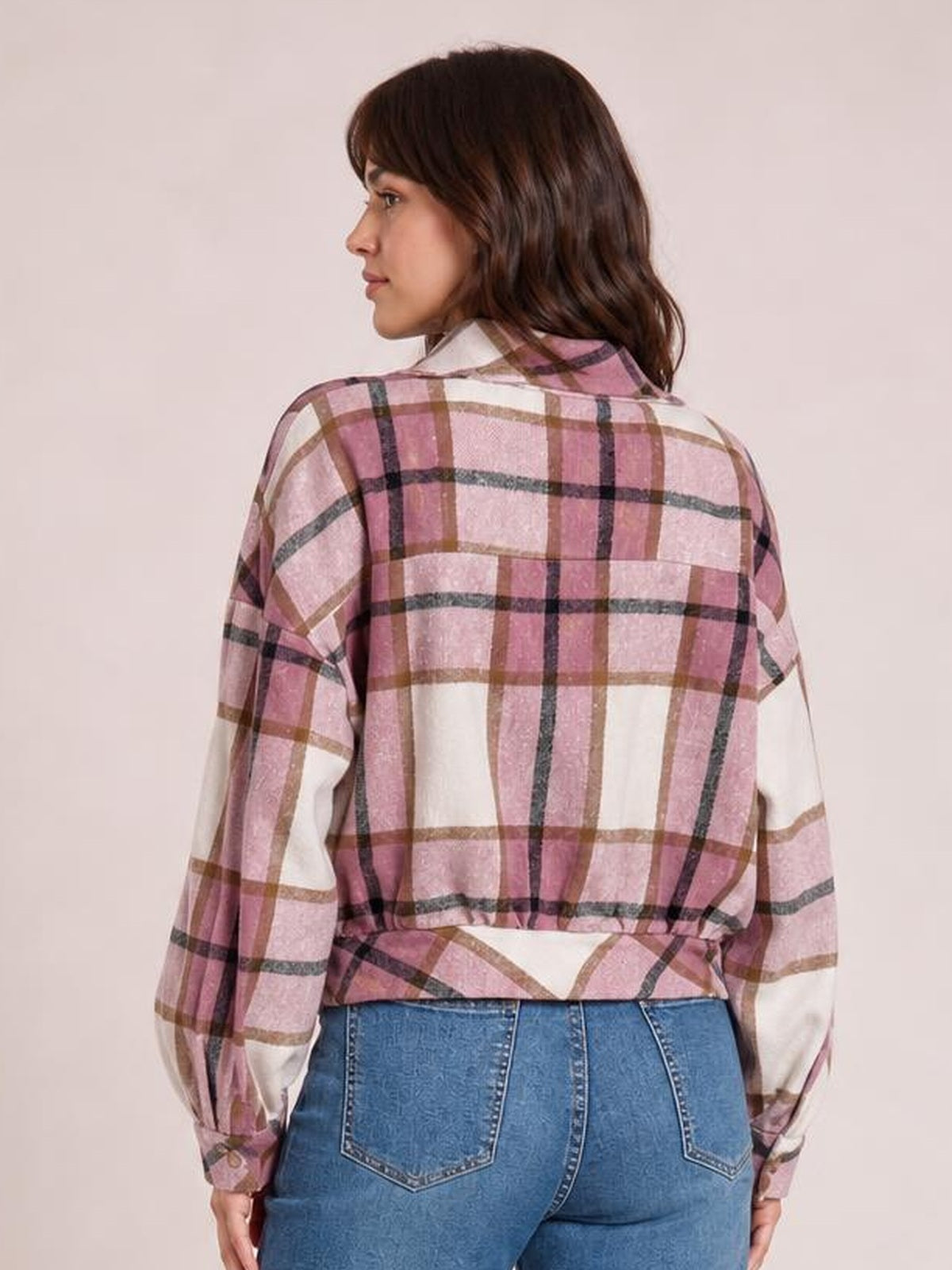A model looks over her shoulder wearing a pink, cream, brown, and black plaid button-up long sleeve jacket with a collared, relaxed silhouette.