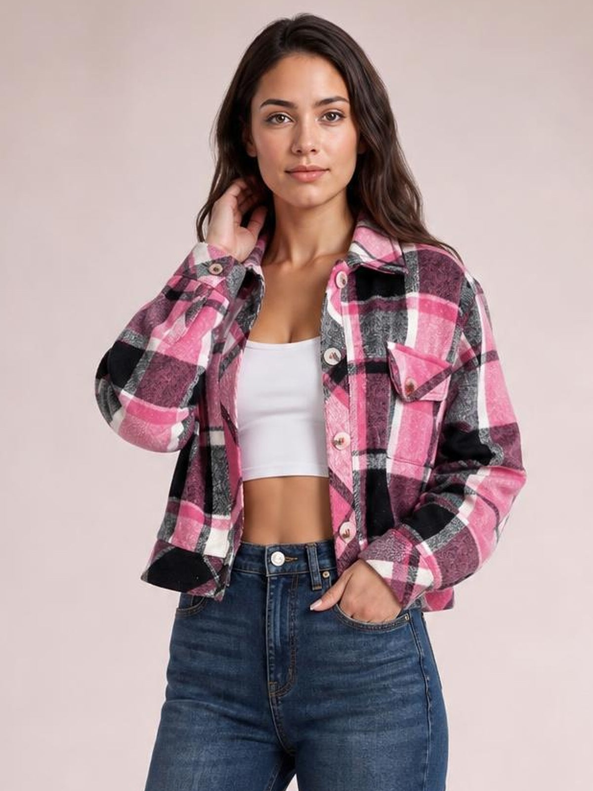 Model poses in a pink, black, gray, and white plaid button-up long sleeve jacket with a collared, relaxed silhouette and flap chest pockets.