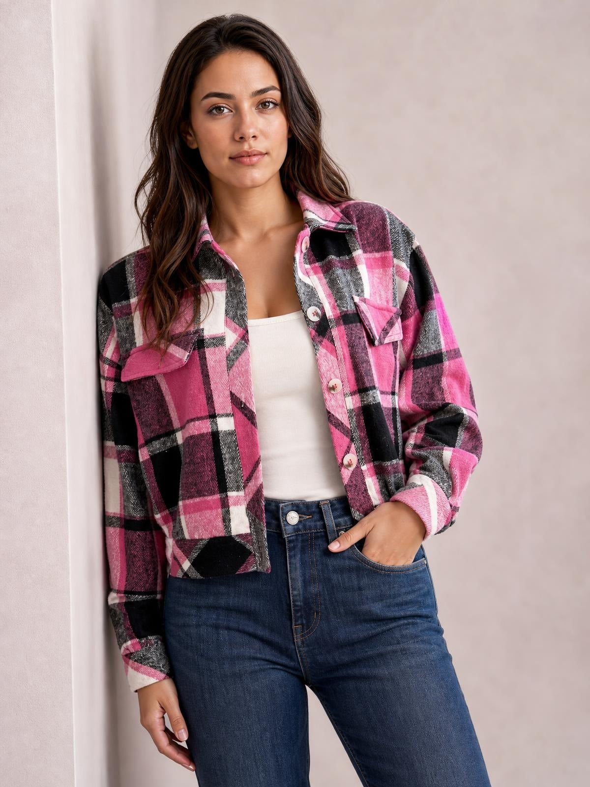 Model wearing a pink, black, and white plaid button-up long sleeve jacket with a cropped silhouette and flap chest pockets, posing with one hand in her jeans pocket.