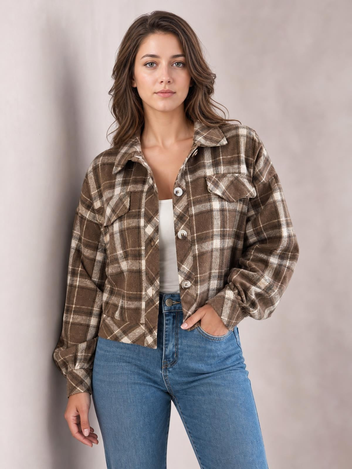 Model wears a brown and cream plaid button-up long sleeve jacket with a collared, relaxed silhouette and flap chest pockets, one hand in a jeans pocket.