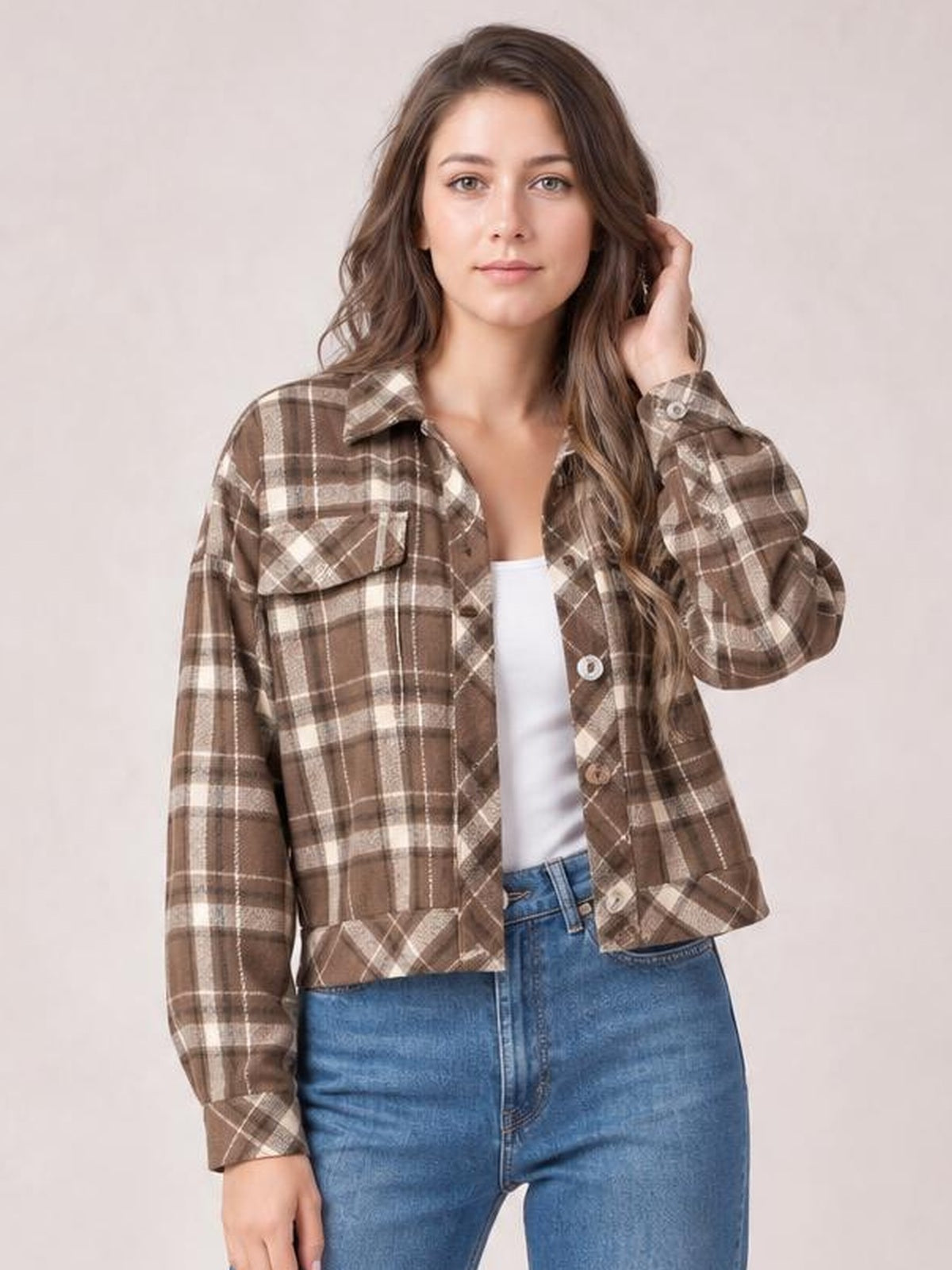 Model wearing a brown plaid button-up long-sleeve jacket with a collared neckline, flap chest pockets, button cuffs, and a relaxed cropped silhouette.