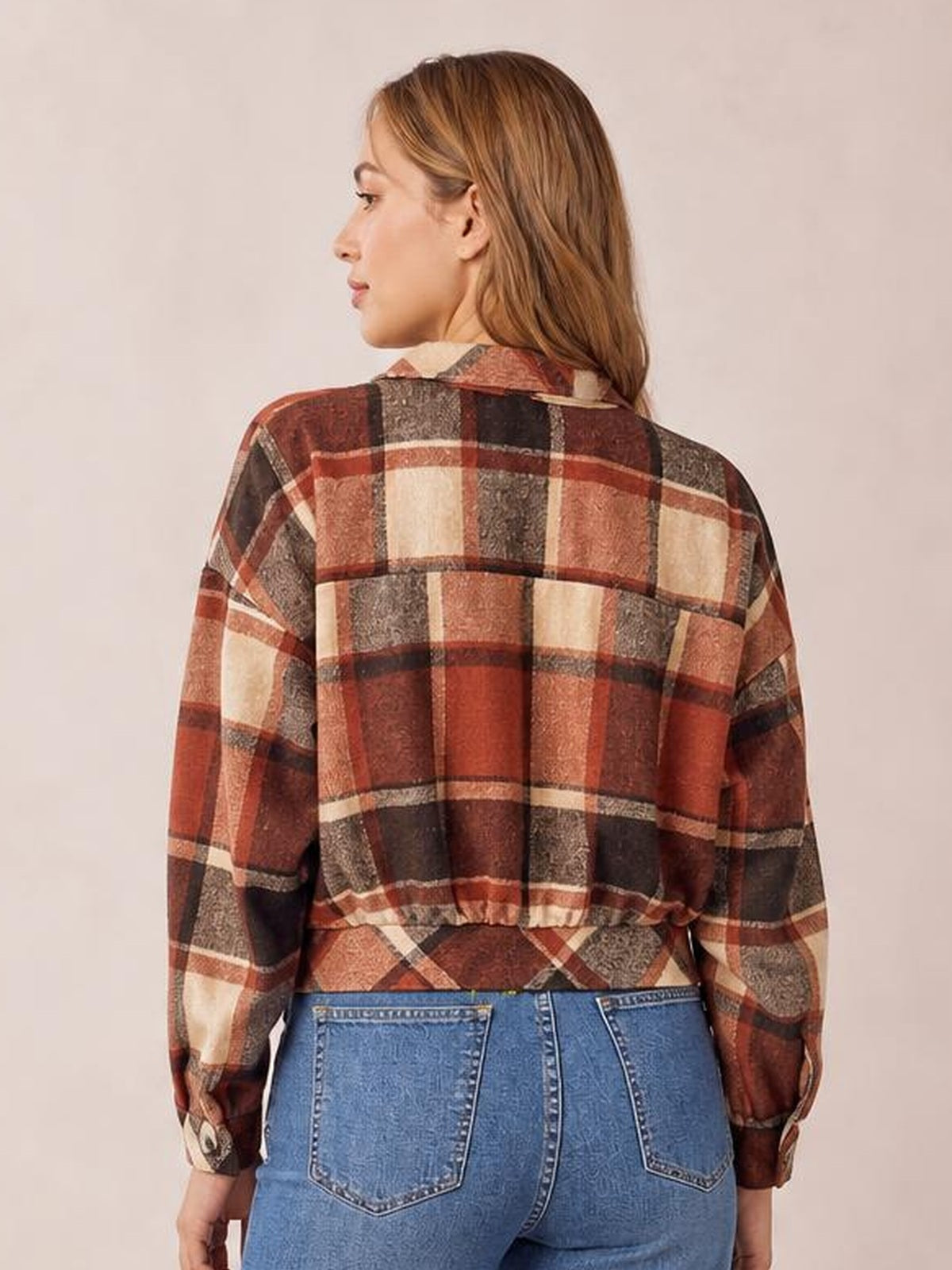 Model seen from behind wearing a rust, brown, cream, and black plaid button-up long sleeve jacket with a relaxed cropped silhouette and collared construction.