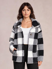 A woman stands wearing a black-and-white plaid collared button-down jacket with long sleeves, a relaxed straight silhouette, and one hand in a pocket.