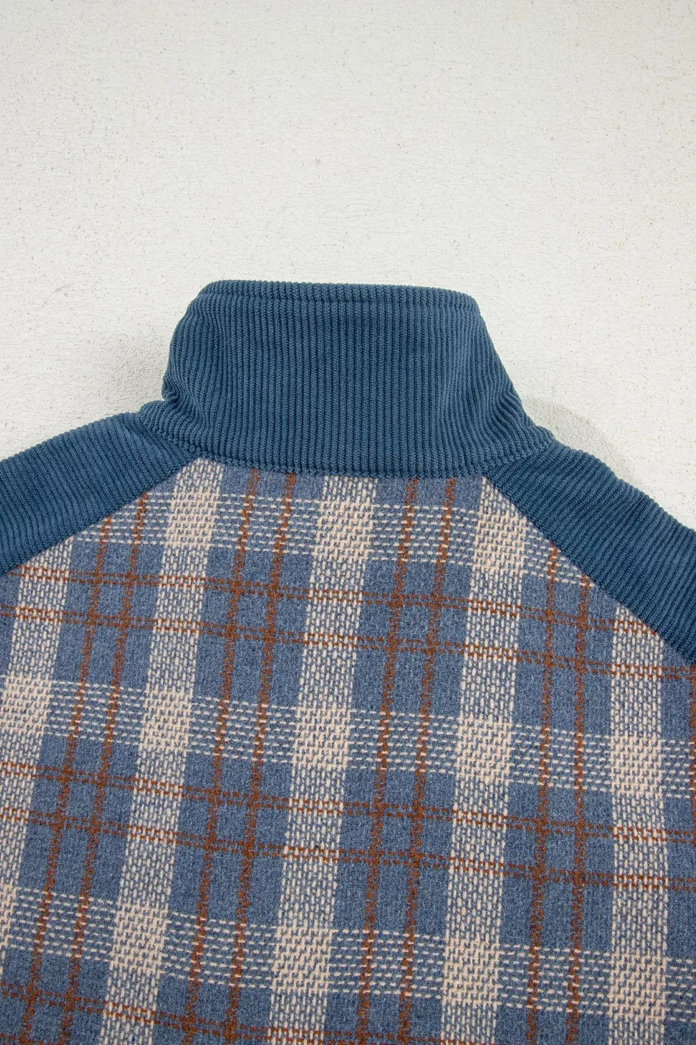 Close-up of a blue corduroy jacket collar and sleeves with a beige, blue, and brown plaid patchwork body showing textured construction.