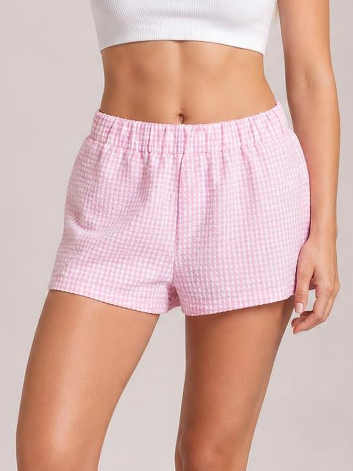 A model wears pink plaid elastic waist shorts with a relaxed silhouette, gathered waistband, straight short hems, and a lightweight woven construction.