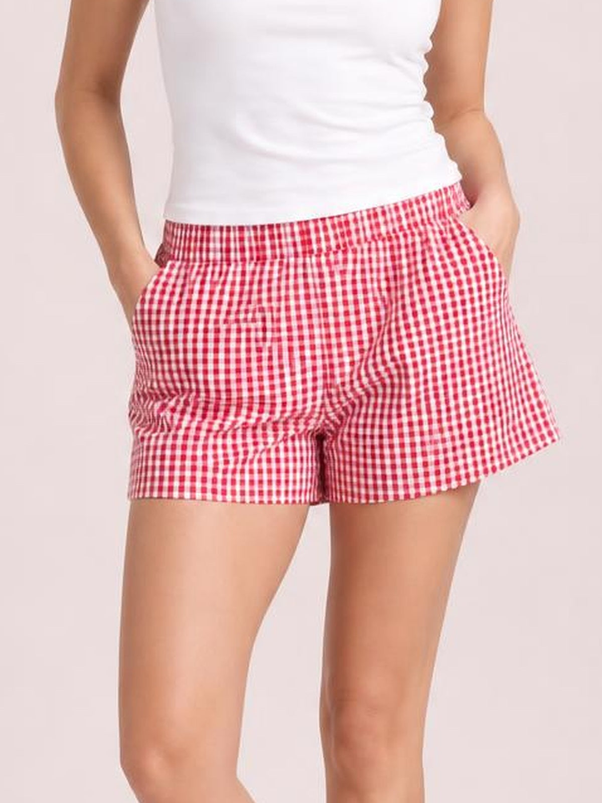 Model wearing red-and-white plaid elastic waist shorts with a relaxed silhouette, side pockets, and straight hems, hands tucked into the pockets.