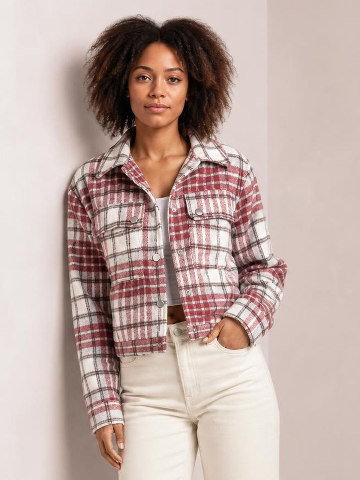 Model poses in a red, white, and black plaid flannel shift jacket with a collar, long sleeves, metal buttons, chest pockets, and a cropped silhouette.