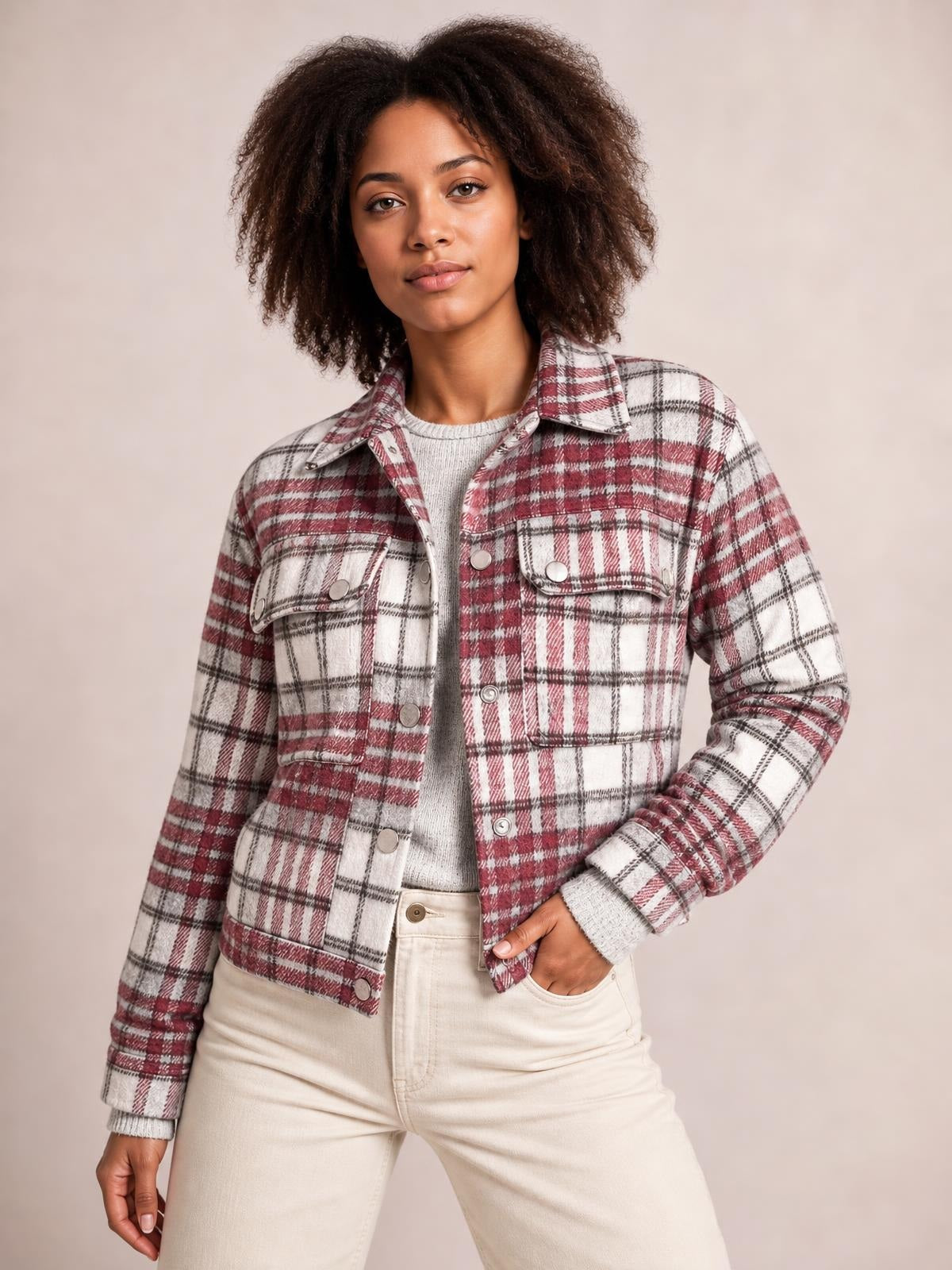 Model wears a burgundy, white, and black plaid flannel shift jacket with a pointed collar, long sleeves, metal buttons, chest pockets, and a relaxed silhouette.