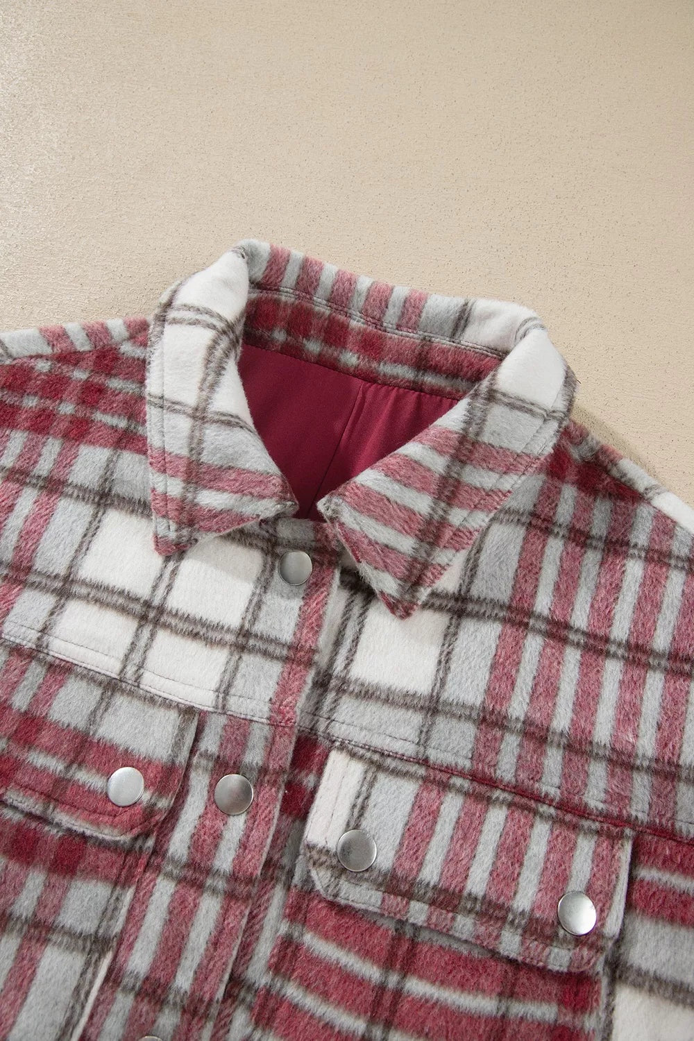 Red, white, and gray plaid flannel shift jacket featuring a pointed collar, metal button closure, long sleeves, and flap pockets.