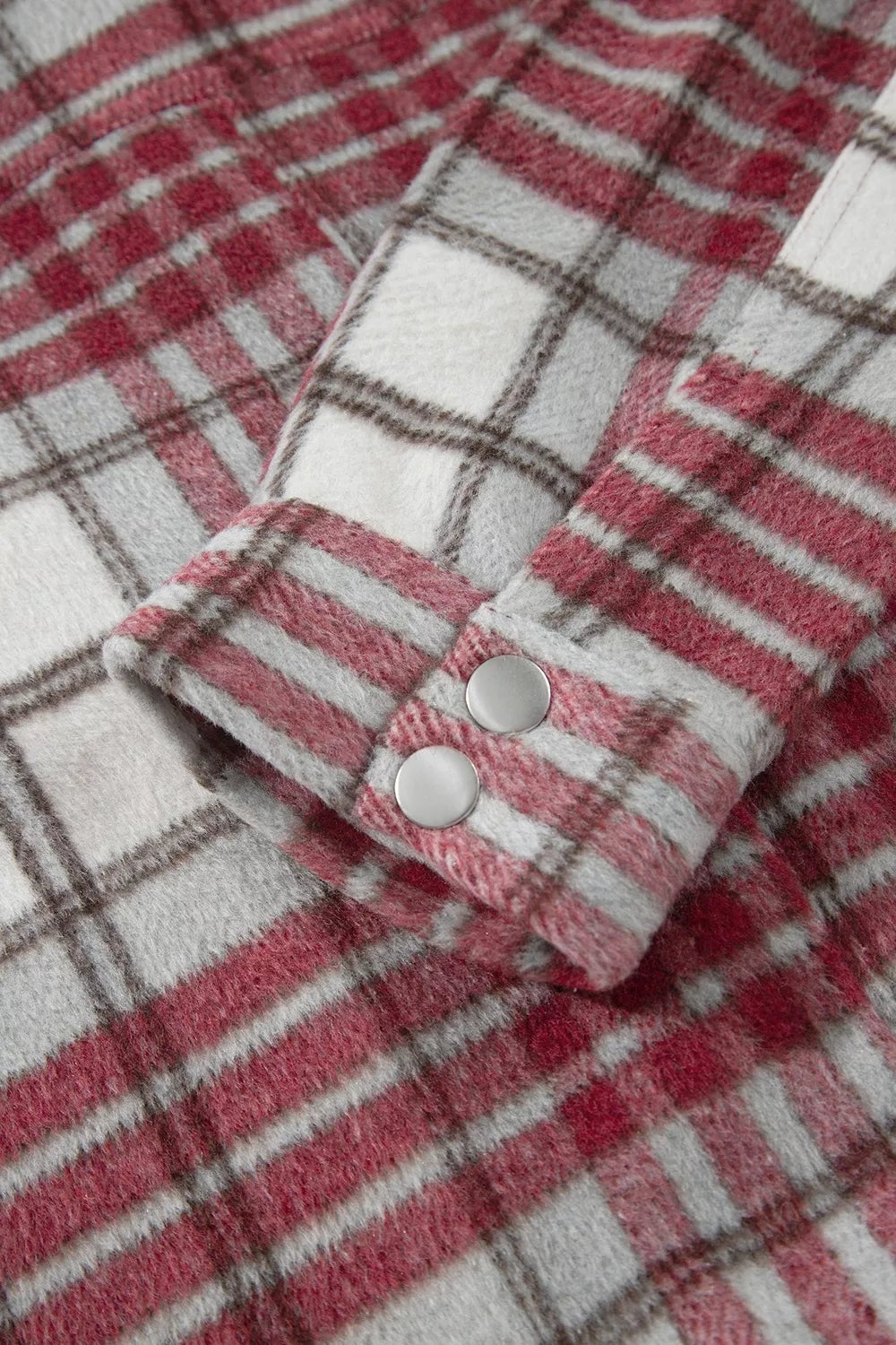 Red, gray, and white plaid flannel jacket close-up showing the soft woven texture, long-sleeve cuff, and two round metal buttons.