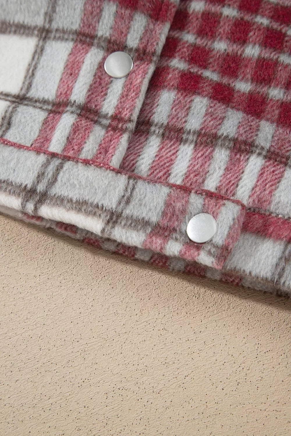 Close-up of a red, white, and gray plaid flannel jacket showing its soft brushed texture, overlapping button placket, and shiny metal buttons.