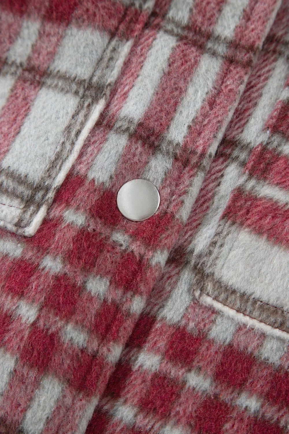 Close-up of a burgundy, gray, and white plaid flannel jacket showing its soft textured fabric, stitching, and round metal button closure.
