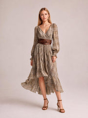 Model wears a taupe plaid high-low long sleeve dress with a ruched wrap bodice, ruffled tiered skirt, and flowing asymmetric hem.