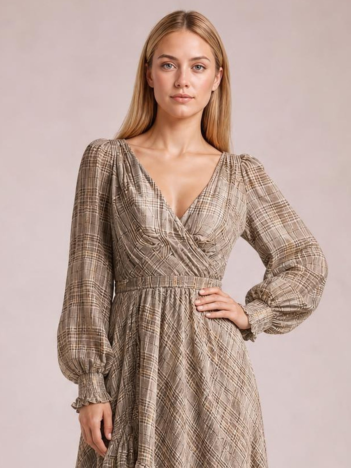 Model poses with one hand on her hip in a taupe plaid long-sleeve dress featuring a wrap V-neck bodice, gathered waist, puff sleeves, and ruffled cuffs.