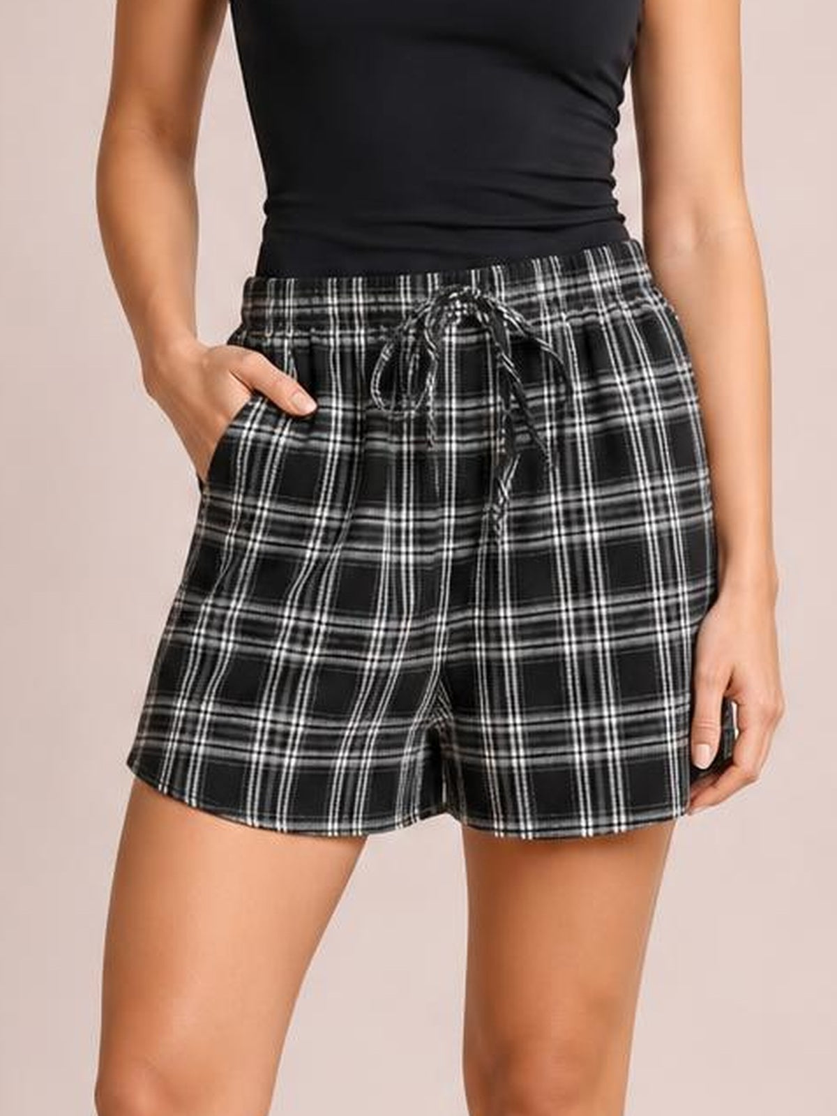 Model wearing black-and-white plaid high-waist shorts with a relaxed silhouette, drawstring waist, side pockets, and straight hems.