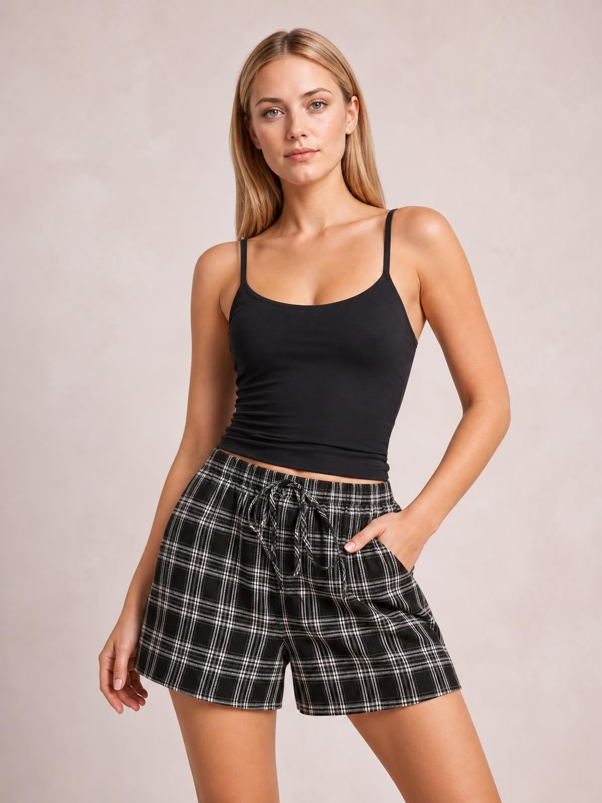 Model poses with one hand in the pocket of black-and-white plaid high waist shorts featuring a relaxed silhouette, drawstring waist, and straight hems.