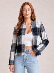 Model wearing a black, gray, and white plaid open-front long sleeve jacket with a cropped straight silhouette over a white top, one hand in her jeans pocket.