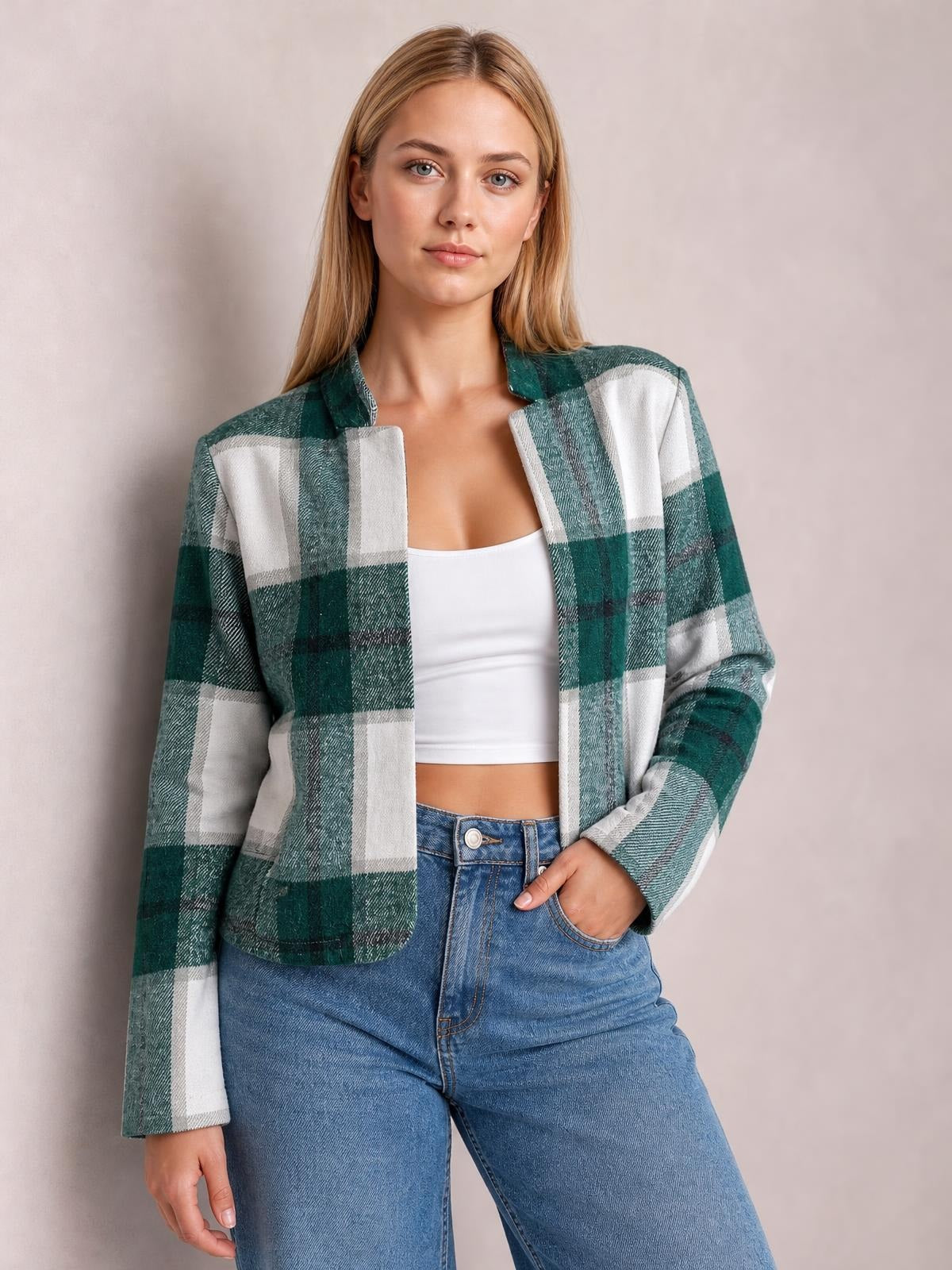 Model wears a green and white plaid open front long sleeve jacket with a relaxed silhouette, rounded hem, and one hand in her jeans pocket.