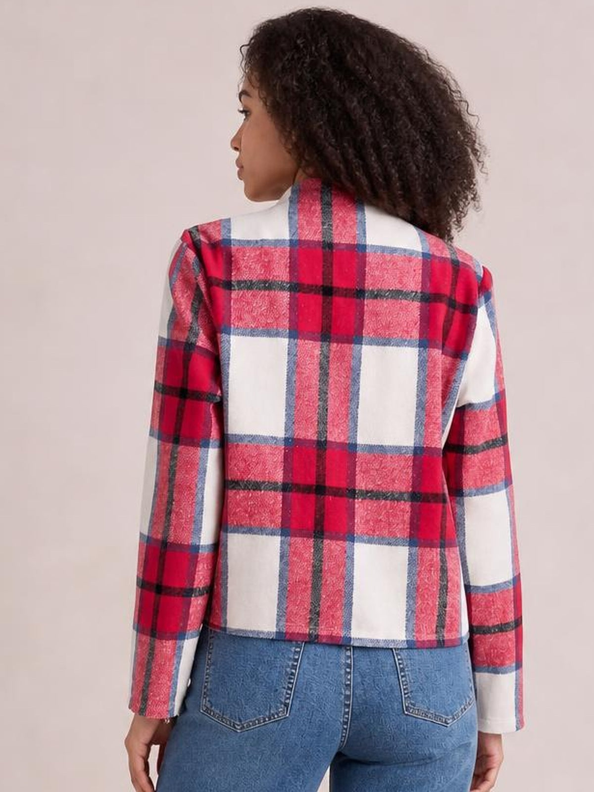 A model faces away, showing the back of a red, white, and blue plaid long-sleeve jacket with a cropped, straight silhouette and tailored shoulder seams.
