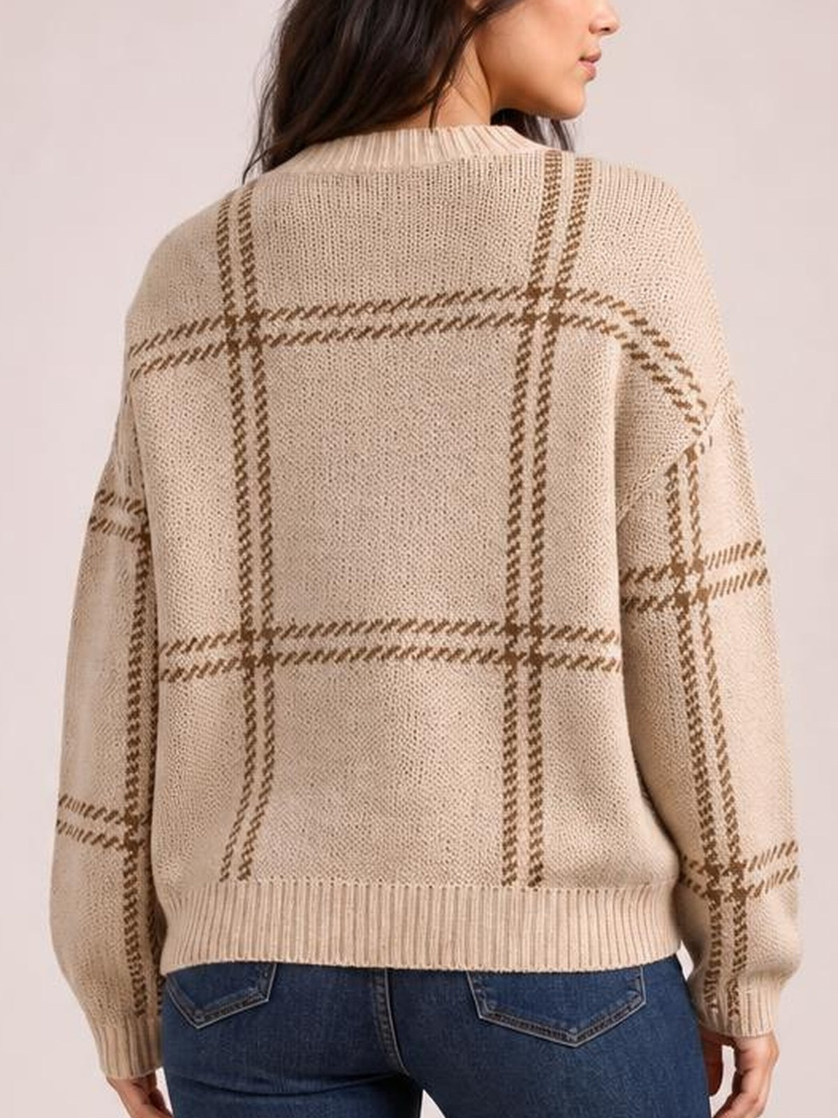 Back view of a model wearing a beige plaid round-neck sweater with dropped shoulders, long sleeves, ribbed cuffs and hem, and a relaxed silhouette.