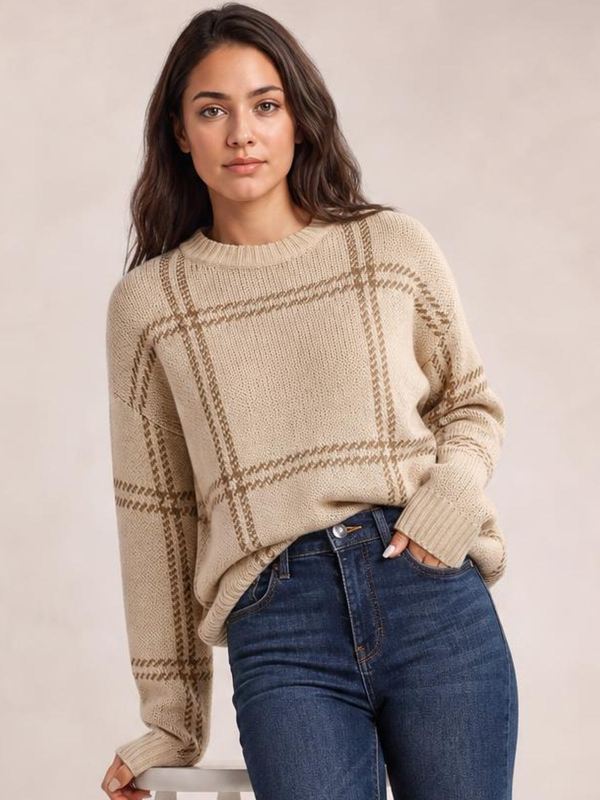 Model wearing a beige plaid round-neck sweater with dropped shoulders, relaxed oversized silhouette, ribbed neckline and cuffs, casually tucked into jeans.