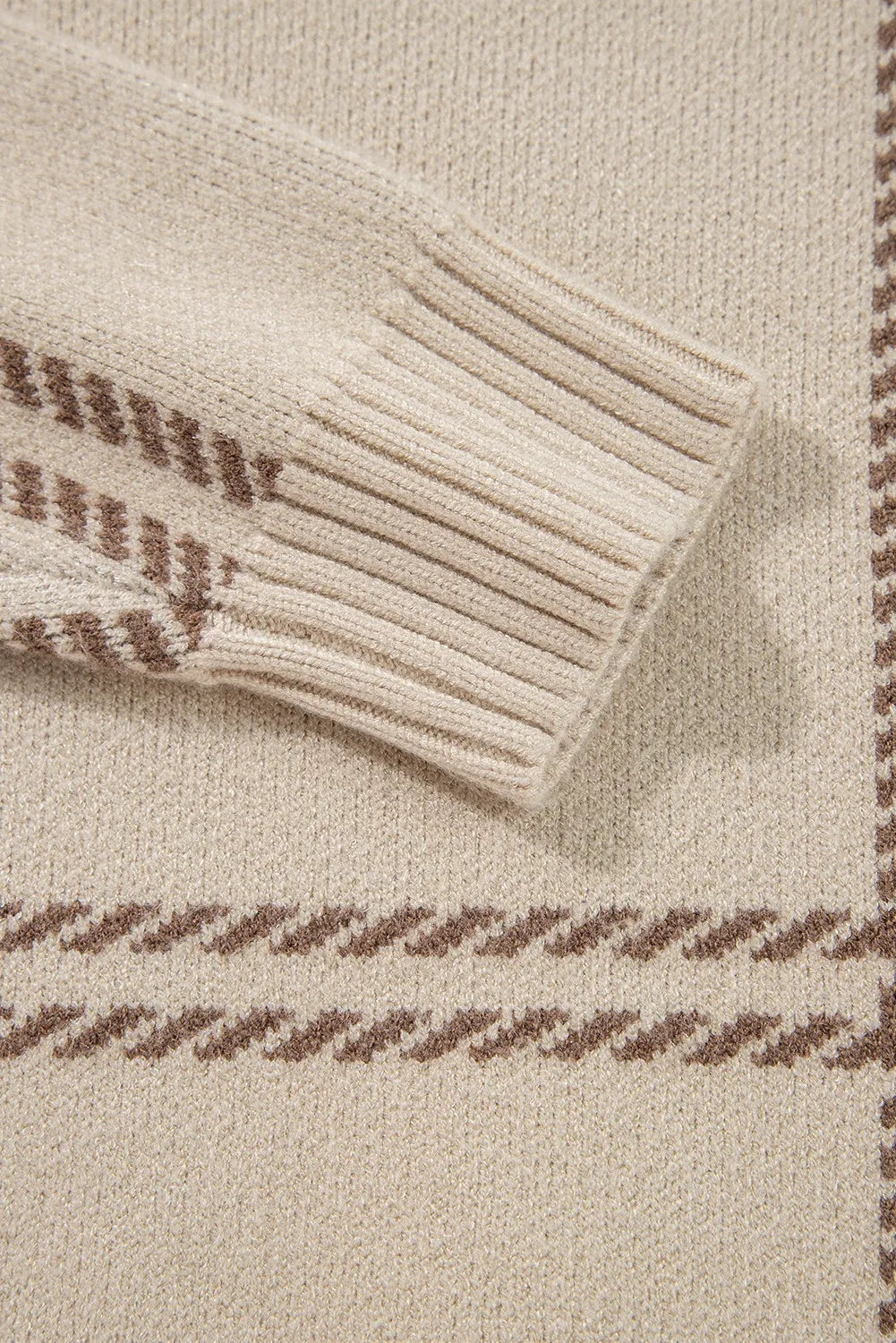Close-up of a cream plaid sweater showing its soft knit texture and ribbed sleeve cuff with subtle brown patterning.