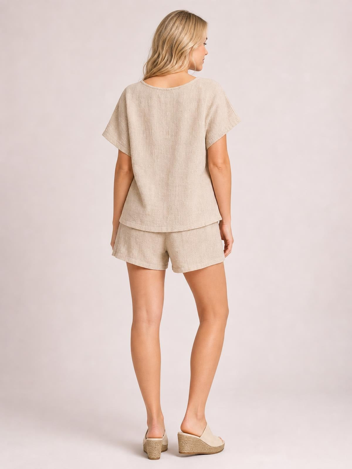 A model stands turned away in a beige short-sleeve top with a relaxed straight silhouette and matching drawstring shorts with a loose fit.
